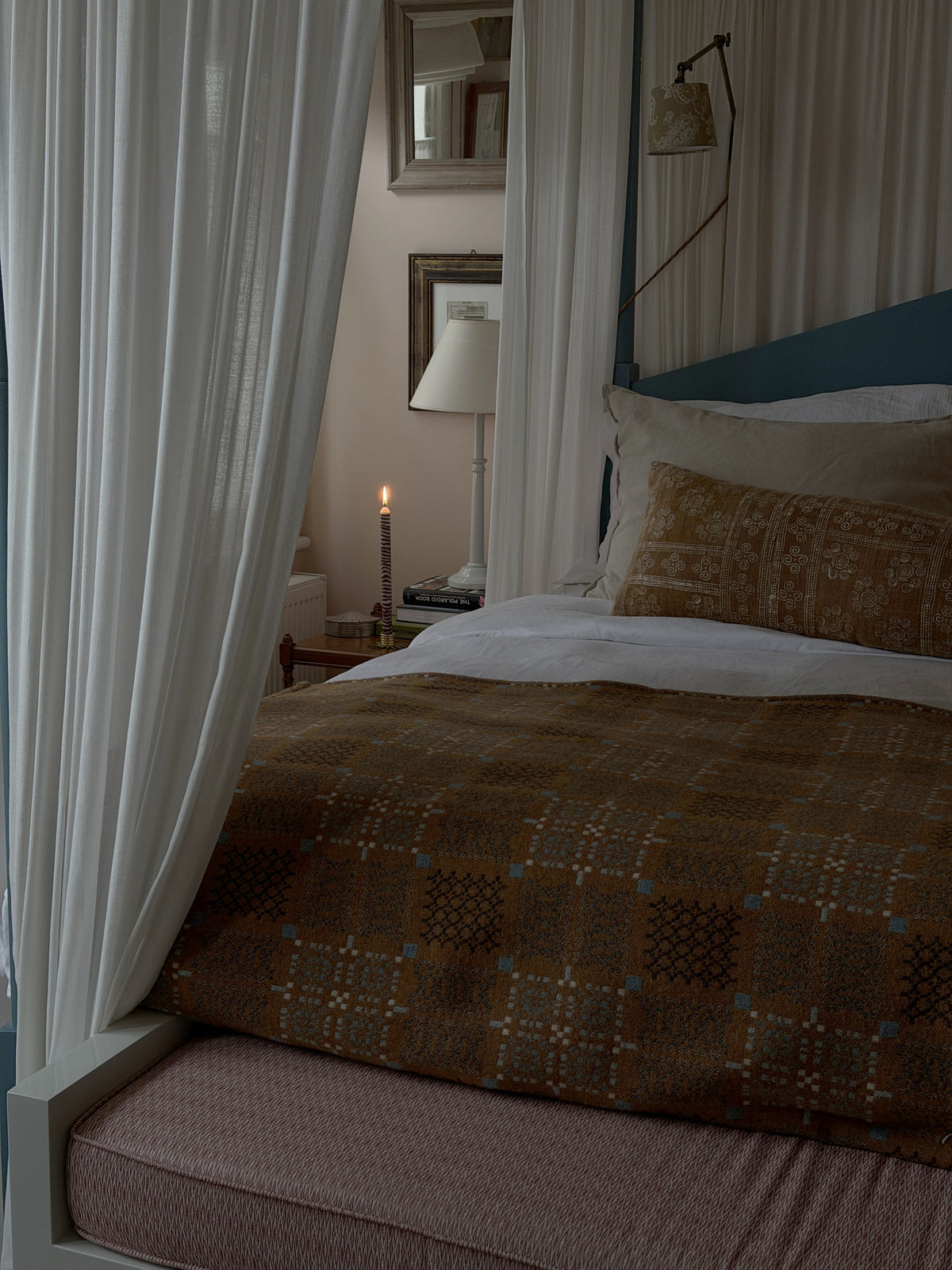 Walnut dinner candle by Pygmalion London glowing on a bedside table beyond a four-poster bed