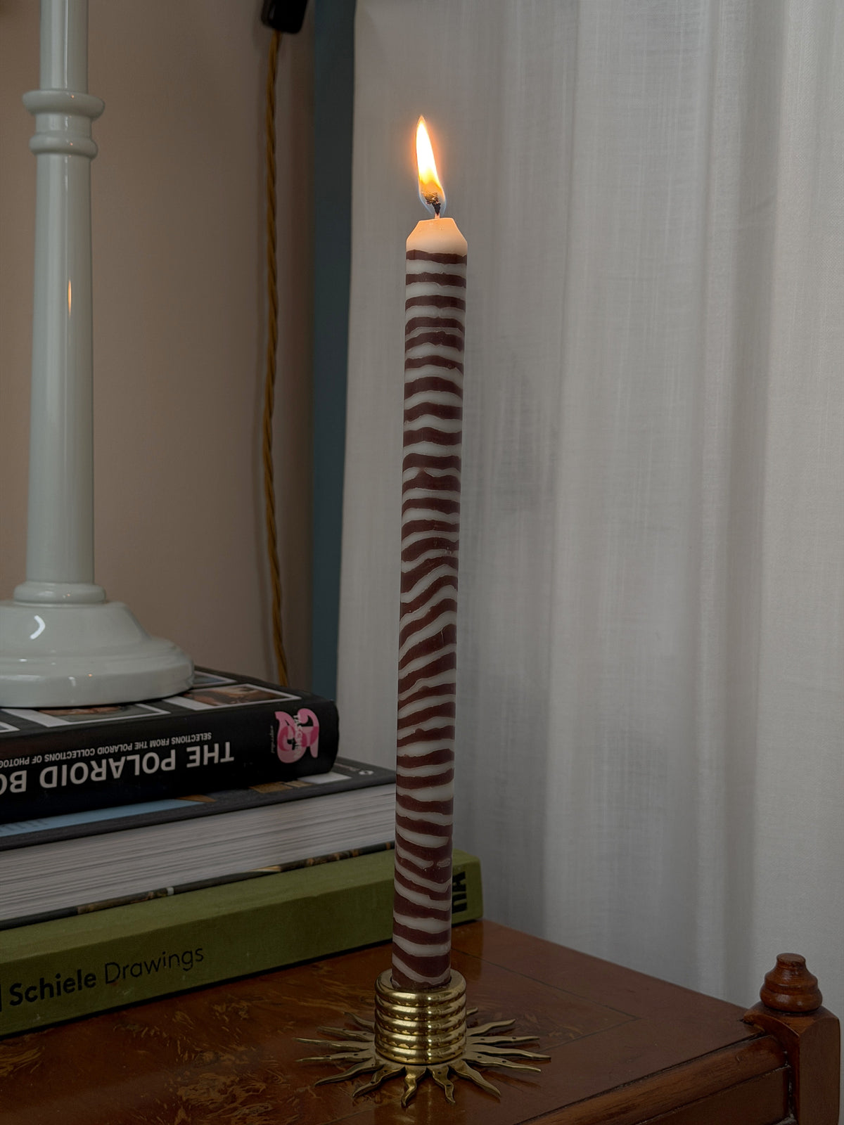 Close-up of a lit Walnut marbled dinner candle by Pygmalion London in a brass sun holder