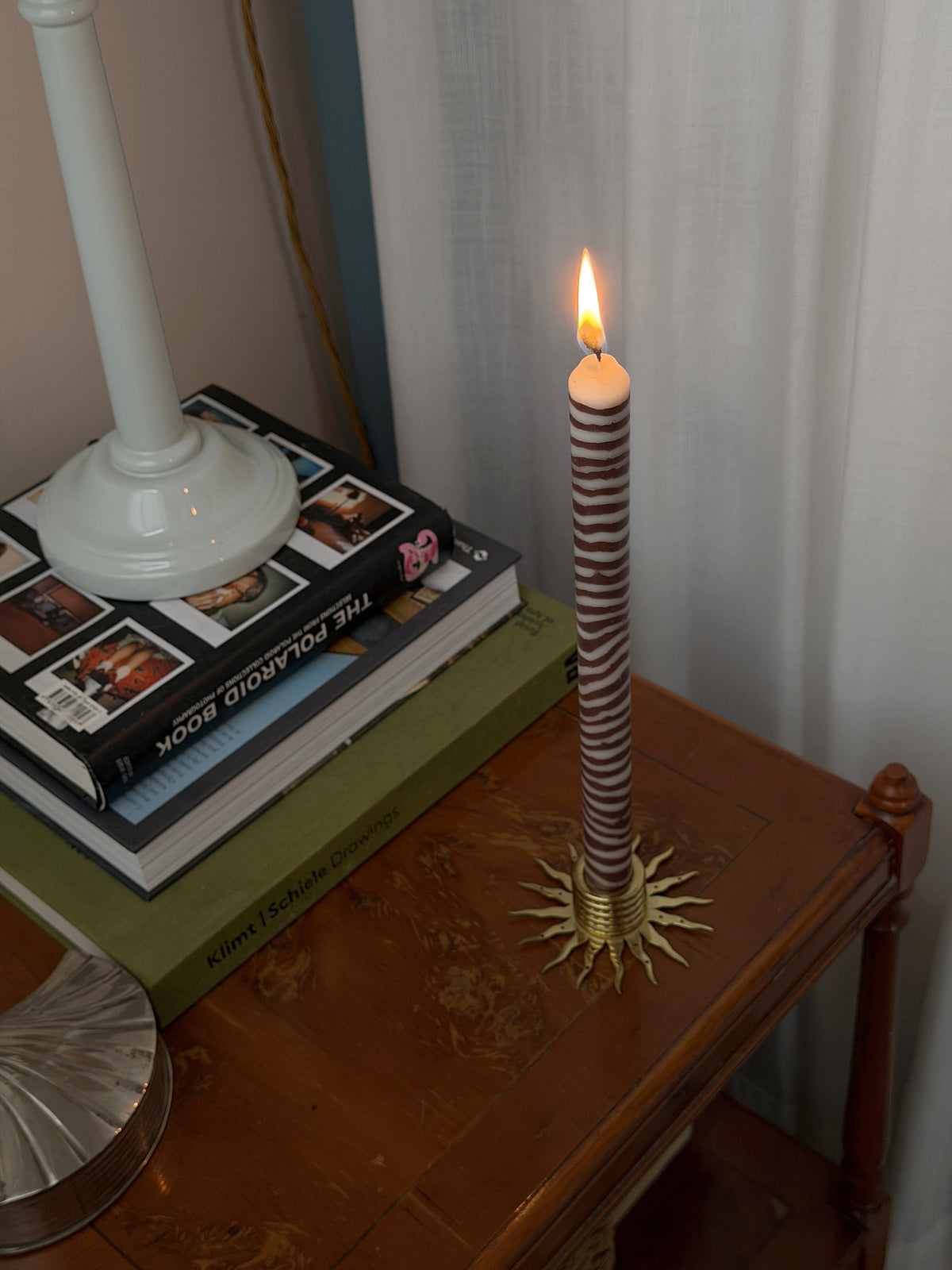 Walnut marbled dinner candle by Pygmalion London, lit on an antique side table with books